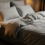 Cama acogedora en una habitación con luz tenue, con un smartphone y auriculares para escuchar sonidos relajantes.
